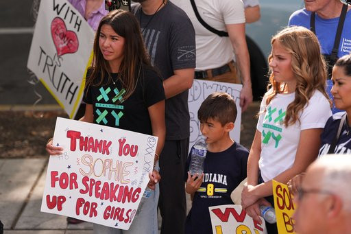 Ahnaleigh Wilson, 17, a track athlete who says she has competed against and placed behind transgender athletes at meets, holds a sign for Indiana Fever guard Sophie Cunningham during a rally before a WNBA basketball game between the Fever and the Seattle Storm, Tuesday, July 28, 2026, in Seattle. (AP Photo/Lindsey Wasson)