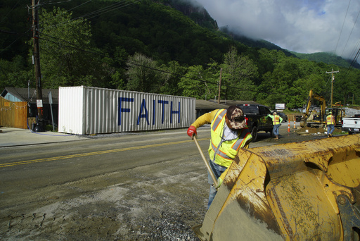 David Cruz mixes cement in the bucket of an end loader for a sewer manhole on Main Street in Chimney Rock Village, N.C., on Wednesday, May 14, 2025. (AP Photo/Allen G. Breed)