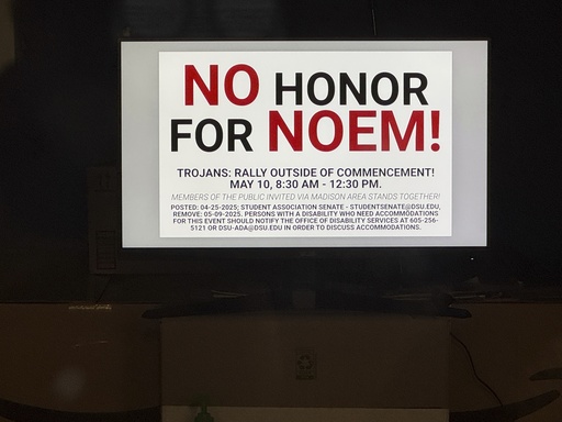 A banner on a television monitor in the student senate office is displayed in Dakota State University's Trojan Center, calling for students to protest Homeland Security Secretary Kristi Noem's commencement speech, Monday, April 28, 2025, in Madison, S.D. (AP Photo/Sarah Raza)