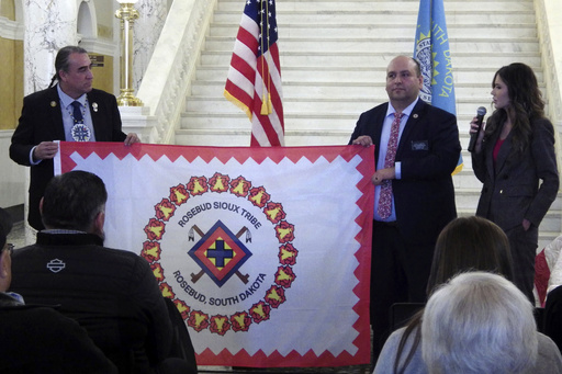 FILE - South Dakota state Democratic Sen. Shawn Bordeaux, left, and Rep. Eric Emery hold the flag of the Rosebud Sioux Tribe on Jan. 10, 2024, at the state Capitol in Pierre, S.D. At right is South Dakota Republican Gov. Kristi Noem. (AP Photo/Jack Dura, file)