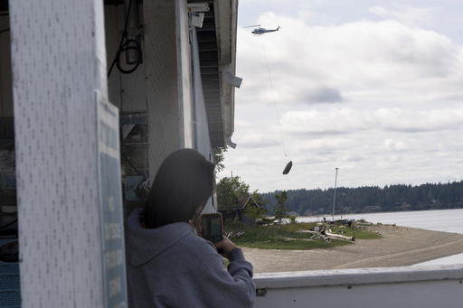 Lucy Trout, from Olympia, Wash., watches as an abandoned ship is transported to shore on Wednesday, June 4, 2025, in Olympia, Wash. (AP Photo/Jenny Kane)
