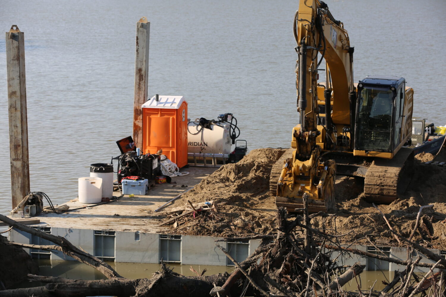 An excavator sits on a floating barge, cleaning sediment and debris from McCook Lake on June 11, 2025. (Joshua Haiar/South Dakota Searchlight)