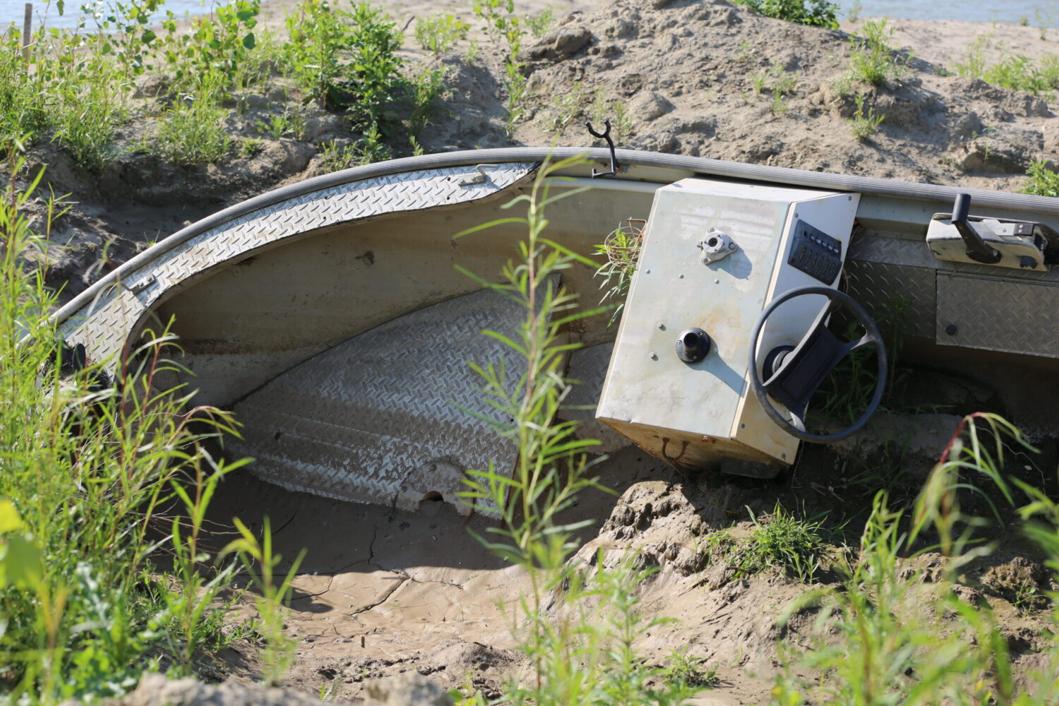 A boat lays in the mud along the shores of McCook Lake on June 11, 2025. (Joshua Haiar/South Dakota Searchlight)