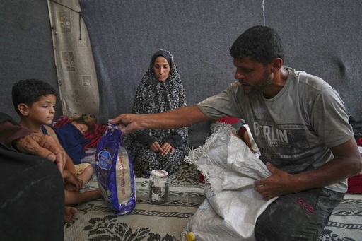 Omar al-Hobi, 43, from Rafah, unpacks a bag of food he collected at a distribution center run by private contractor the Gaza Humanitarian Foundation in the southern Gaza Strip, as he arrives at his family's tent in Khan Younis, Tuesday, June 10, 2025. At left are his children and his wife, Anwaar Saleh.(AP Photo/Abdel Kareem Hana)