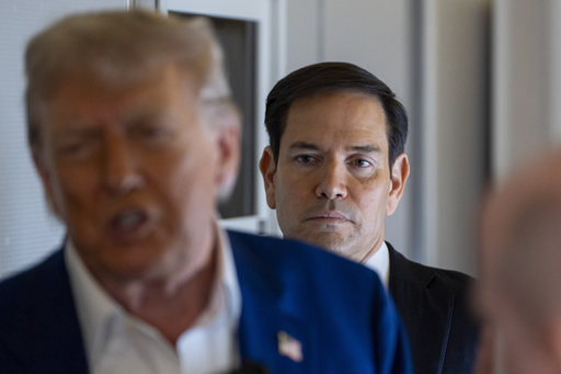 Secretary of State Marco Rubio stands behind as President Donald Trump speaks with reporters on Air Force One while in flight from Joint Base Andrews, Md., to Amsterdam, Netherlands, Tuesday, June 24, 2025. (AP Photo/Alex Brandon)
