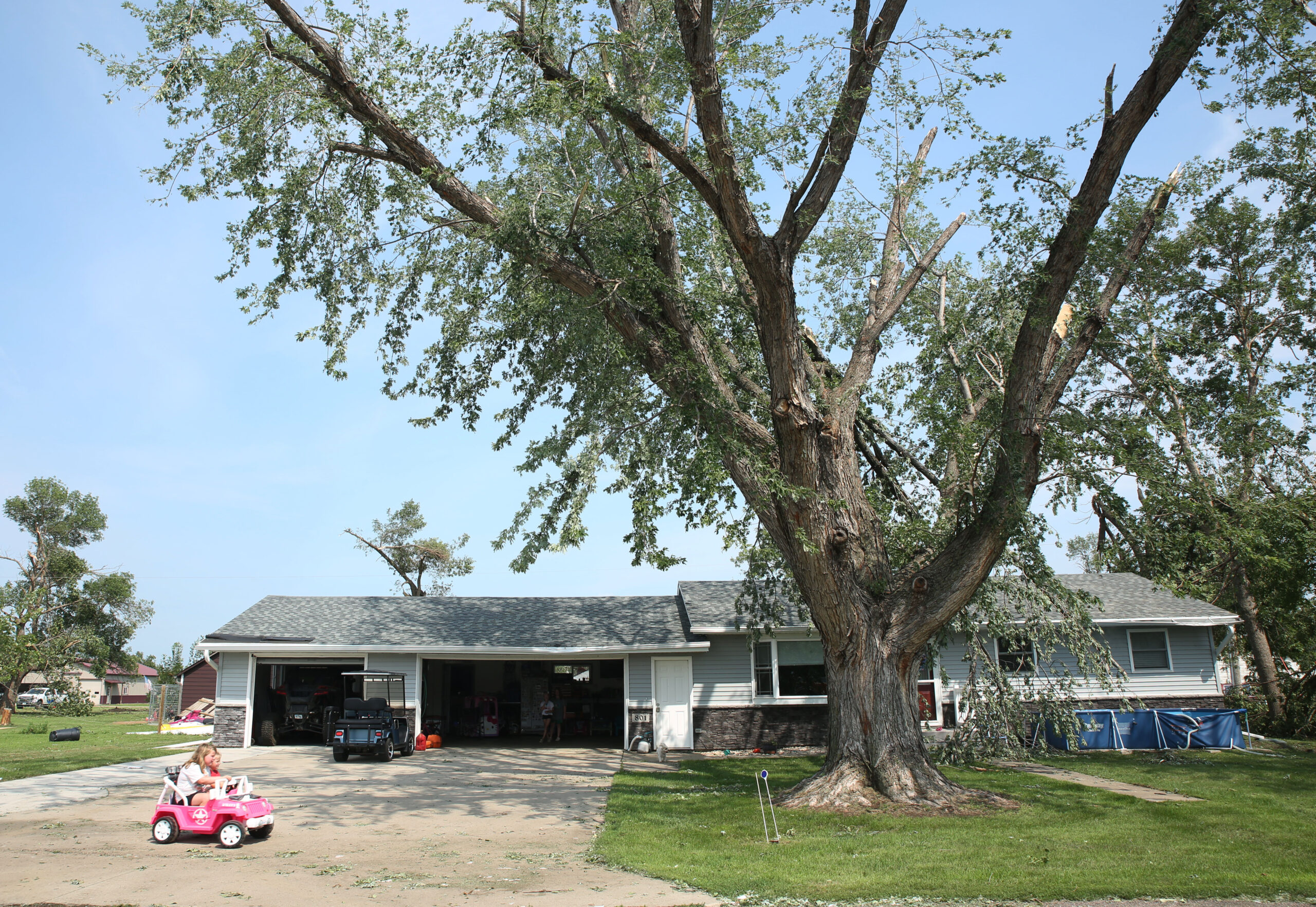 Neighborhood children play in a driveway as volunteers help clean up tree debris in Hudson on Tuesday, July 29, 2025 after severe weather moved through the area Monday evening. The system damaged trees, homes and other structures. (Makenzie Huber/South Dakota Searchlight)