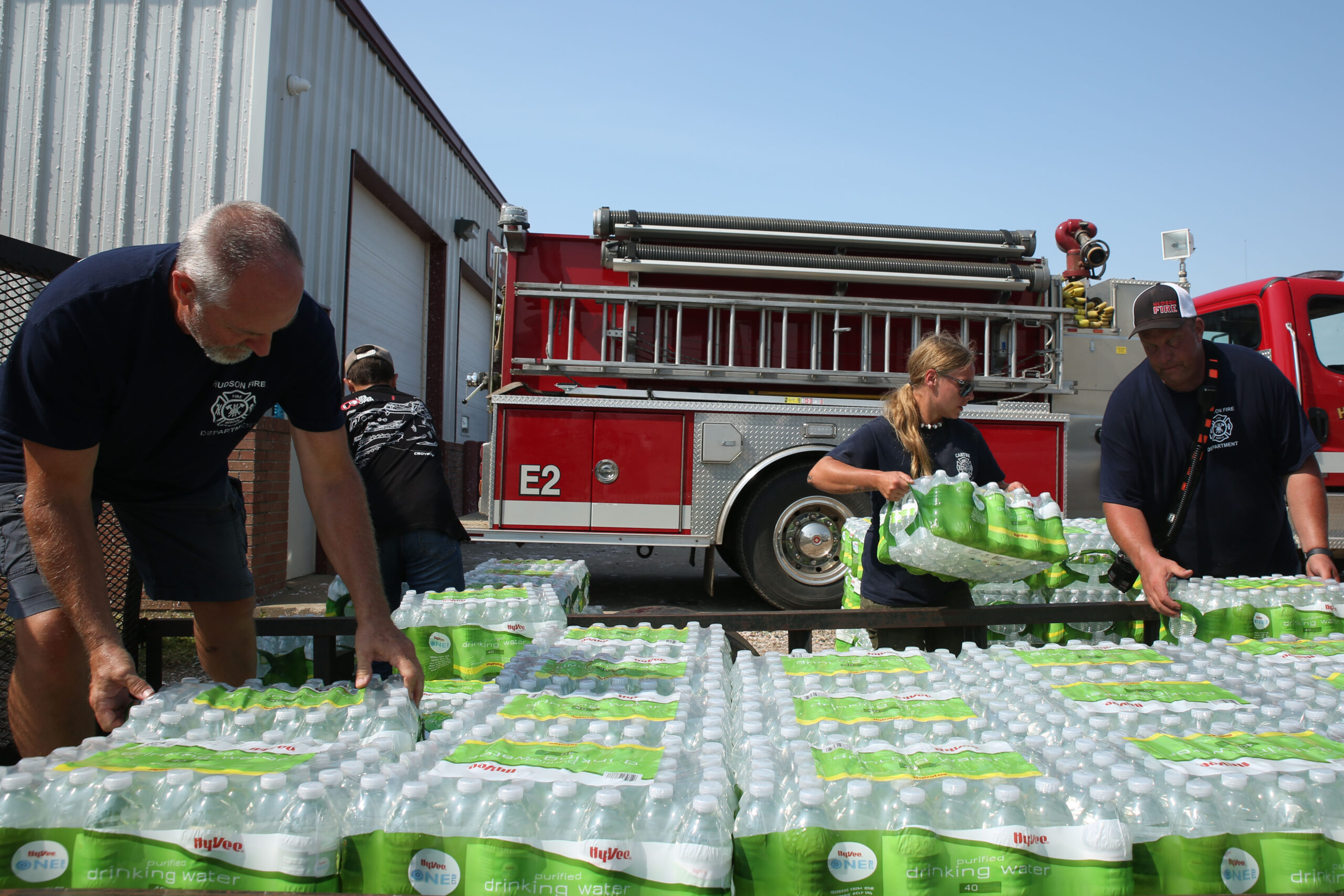 Hudson volunteer firefighters offload bottles of water from a trailer on Tuesday, July 29, 2025 outside of the town's city office and fire department building. A storm moved through the area on Monday evening, damaging trees, homes and other structures. (Makenzie Huber/South Dakota Searchlight)