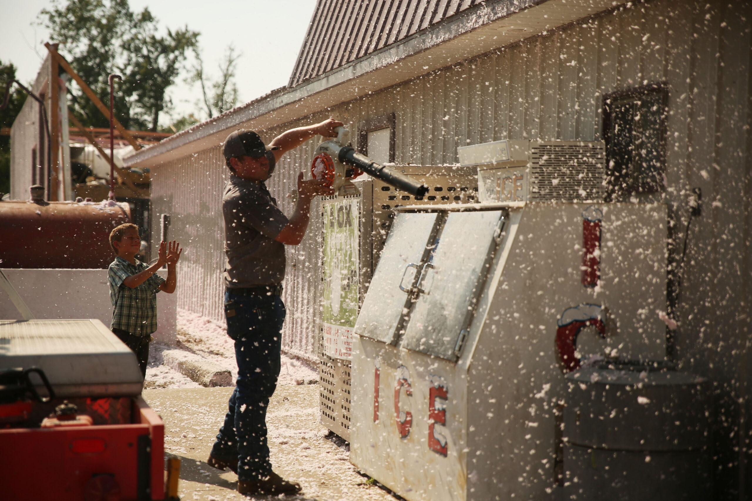 Anson Sadler and his younger brother Clark clear off fiber glass insulation from their family's Fillin' Station business on Tuesday, July 29, 2025. Their warehouse's roof was blown off by a wind storm that moved through the area on Monday evening. The system damaged trees, homes and other structures. (Makenzie Huber/South Dakota Searchlight)