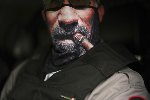 An immigration official wears a face mask depicting a cigar and beard as he waits to transport detained immigrants Wednesday, July 23, 2025, in Baldwin Park, Calif. (AP Photo/Gregory Bull)