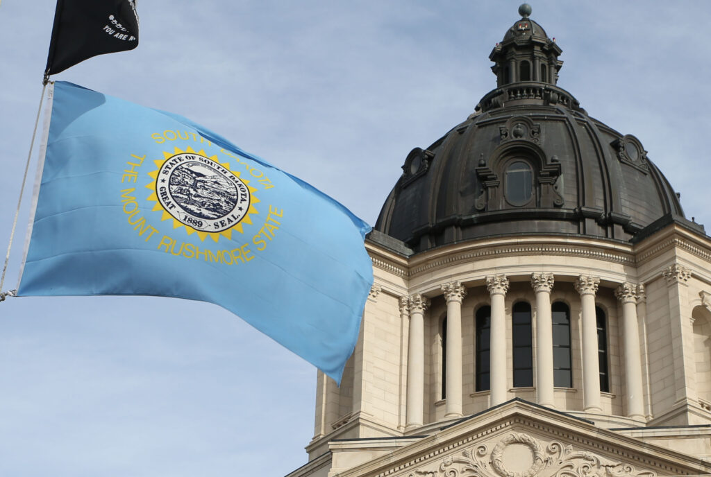 The state flag flies in front of the South Dakota Capitol in Pierre. (Makenzie Huber/South Dakota Searchlight)