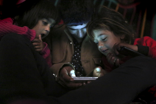 FILE - Children from Yazidi families, displaced by Islamic State group militants, look at a smartphone in a partially constructed building in Dohuk, northern Iraq, Dec. 10, 2014. (AP Photo/Seivan Selim, File)