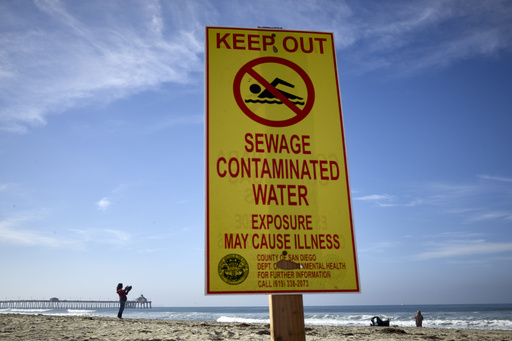 FILE - A woman records with a phone along the beach as a sign warns of contaminated water Dec. 12, 2018, at Imperial Beach, Calif. (AP Photo/Gregory Bull, File)