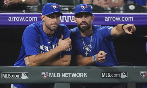 Toronto Blue Jays pitcher Max Scherzer, left,talks with assistant hitting coach Hunter Mense as they look on in the ninth inning of a baseball game against the Colorado Rockies, Monday, Aug. 4, 2025, in Denver. (AP Photo/David Zalubowski)