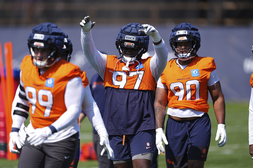 Denver Broncos defensive tackle Malcolm Roach, center, raises his arms to acknowledge the applause of fans while warming up between defensive end Zach Allen, front, and defensive tackle Jordan Miller during an NFL football practice Friday, July 25, 2025, in Centennial, Colo. (AP Photo/David Zalubowski)