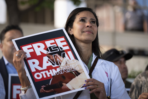 Dr. Wafaa Alrashid, center, whose husband, Rami Othmane, a Tunisian musician, is detained at the U.S. Immigration and Customs Enforcement facility, holds a sign during a rally outside the facility in Los Angeles Friday, July 25, 2025. (AP Photo/Jae C. Hong)