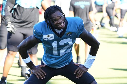Jacksonville Jaguars wide receiver Travis Hunter (12) smiles at photographers as he warms up during practice at the team's NFL football training camp, Monday, July 28, 2025, in Jacksonville, Fla. (AP Photo/John Raoux)