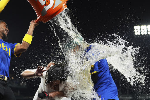Seattle Mariners' Julio Rodriguez, left, douses Root Sports' Jen Mueller and J.P. Crawford, right, after Crawford hit a game-winning two-run home run against the Texas Rangers in a baseball game Friday, Aug. 1, 2025, in Seattle. (AP Photo/Lindsey Wasson)