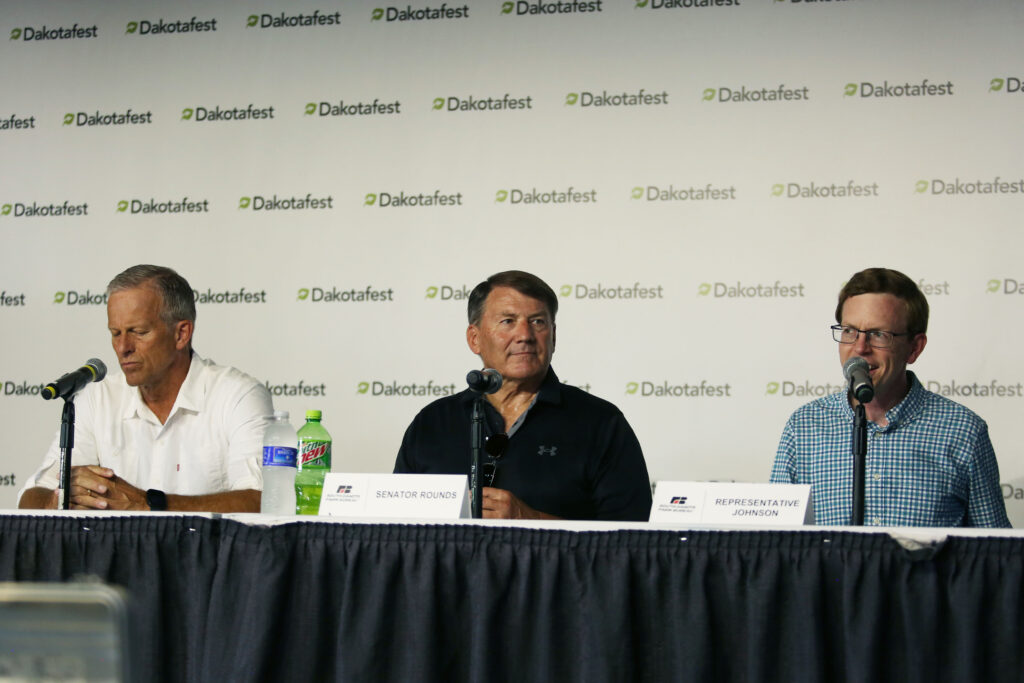 South Dakota Republican congressional delegates, from left, Senate Majority Leader John Thune, Sen. Mike Rounds and Rep. Dusty Johnson speak at Dakotafest in Mitchell on Aug. 20, 2025. (Makenzie Huber/South Dakota Searchlight)