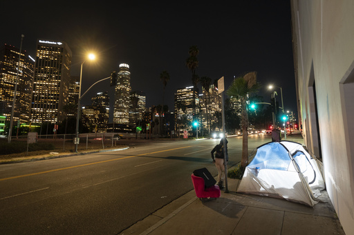 FILE - In this photo illuminated by an off-camera flash, a woman walks past a homeless person's tent with a chair in downtown Los Angeles, Feb. 16, 2023. (AP Photo/Jae C. Hong, File)