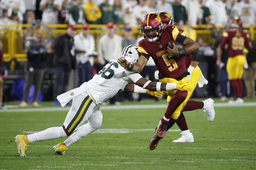 Washington Commanders quarterback Jayden Daniels (5) runs with the ball as Green Bay Packers linebacker Edgerrin Cooper (56) defends during the first half of an NFL football game Thursday, Sept. 11, 2025, in Green Bay, Wis. (AP Photo/Mike Roemer)