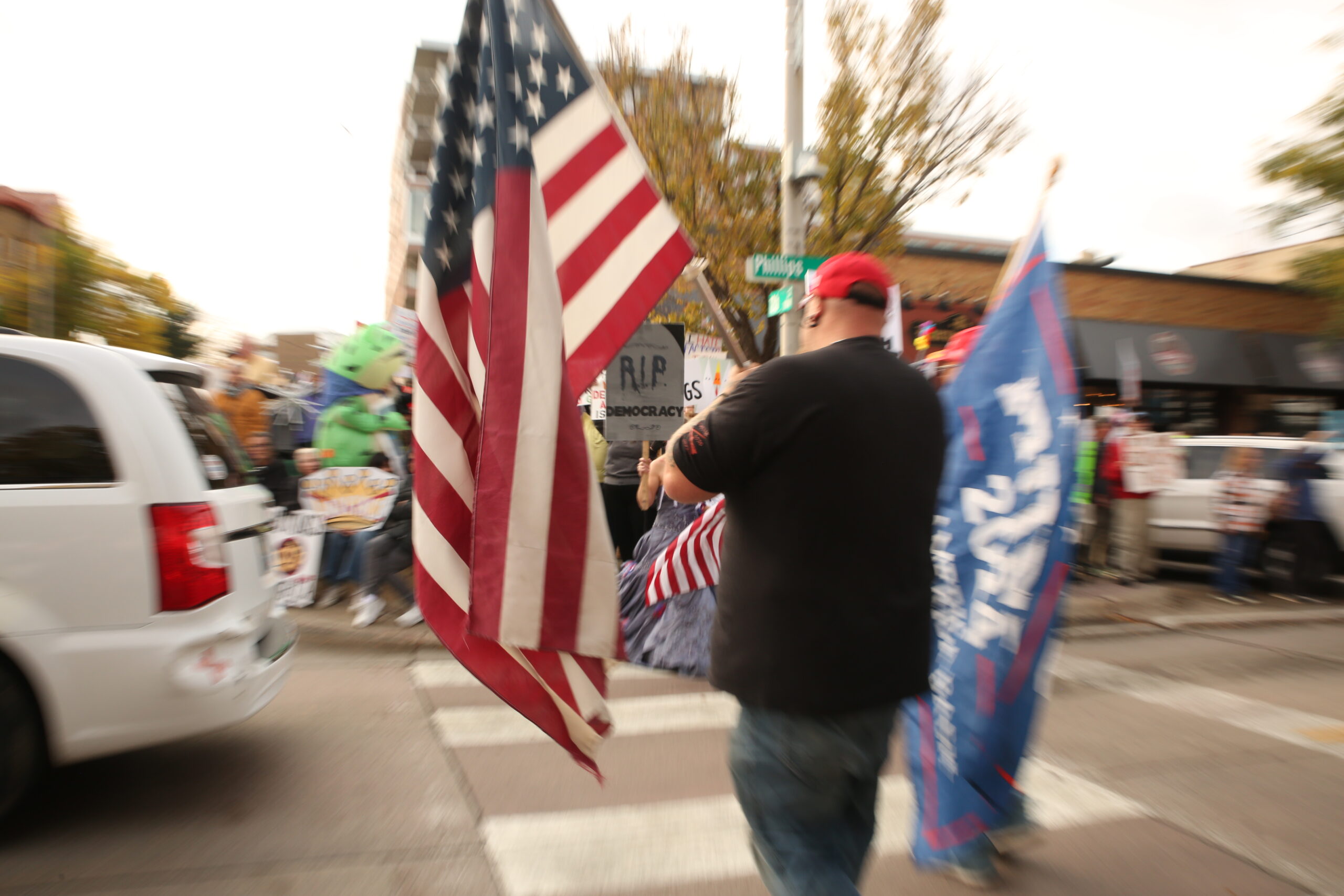 Trump supporters walk through crowds booing them at the No Kings protest in downtown Sioux Falls on Oct. 18, on their way to the Real American Rally nearby. (Photo by Makenzie Huber/South Dakota Searchlight)