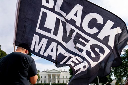 FILE - A man carries a Black Lives Matter flag in Lafayette Square outside the White House on the fourth night of the Republican National Convention, Aug. 27, 2020, in Washington. (AP Photo/Andrew Harnik, File)