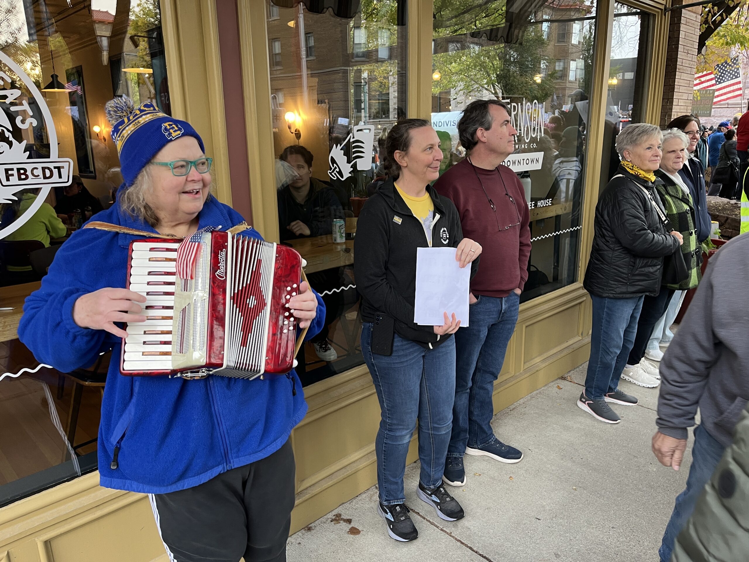 Nancy Lenander plays an accordion for protesters at the No Kings protest in downtown Sioux Falls on Oct. 18, 2025. (Makenzie Huber/South Dakota Searchlight)