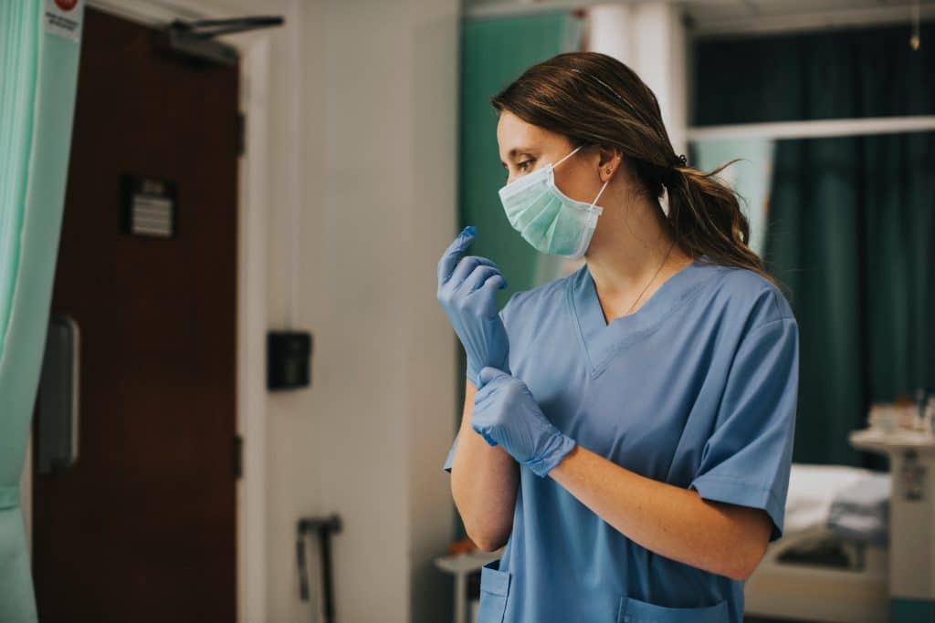 Female nurse with a mask putting on gloves