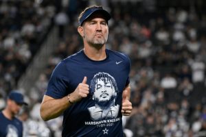 Dallas Cowboys head coach Brian Schottenheimer wears a tribute t-shirt of Cowboys' Marshawn Kneeland prior to an NFL football game against the Las Vegas Raiders Monday, Nov. 17, 2025, in Las Vegas, in memory of Kneeland who passed away earlier this month. (AP Photo/David Becker)
