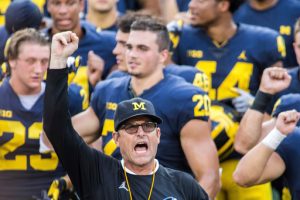 FILE - In this Aug. 26, 2018, file photo, Michigan head coach Jim Harbaugh leads his players and fans in singing "Hail to the Victors" after a practice session by the NCAA college football team at Michigan Stadium in Ann Arbor, Mich..(AP Photo/Tony Ding, File)