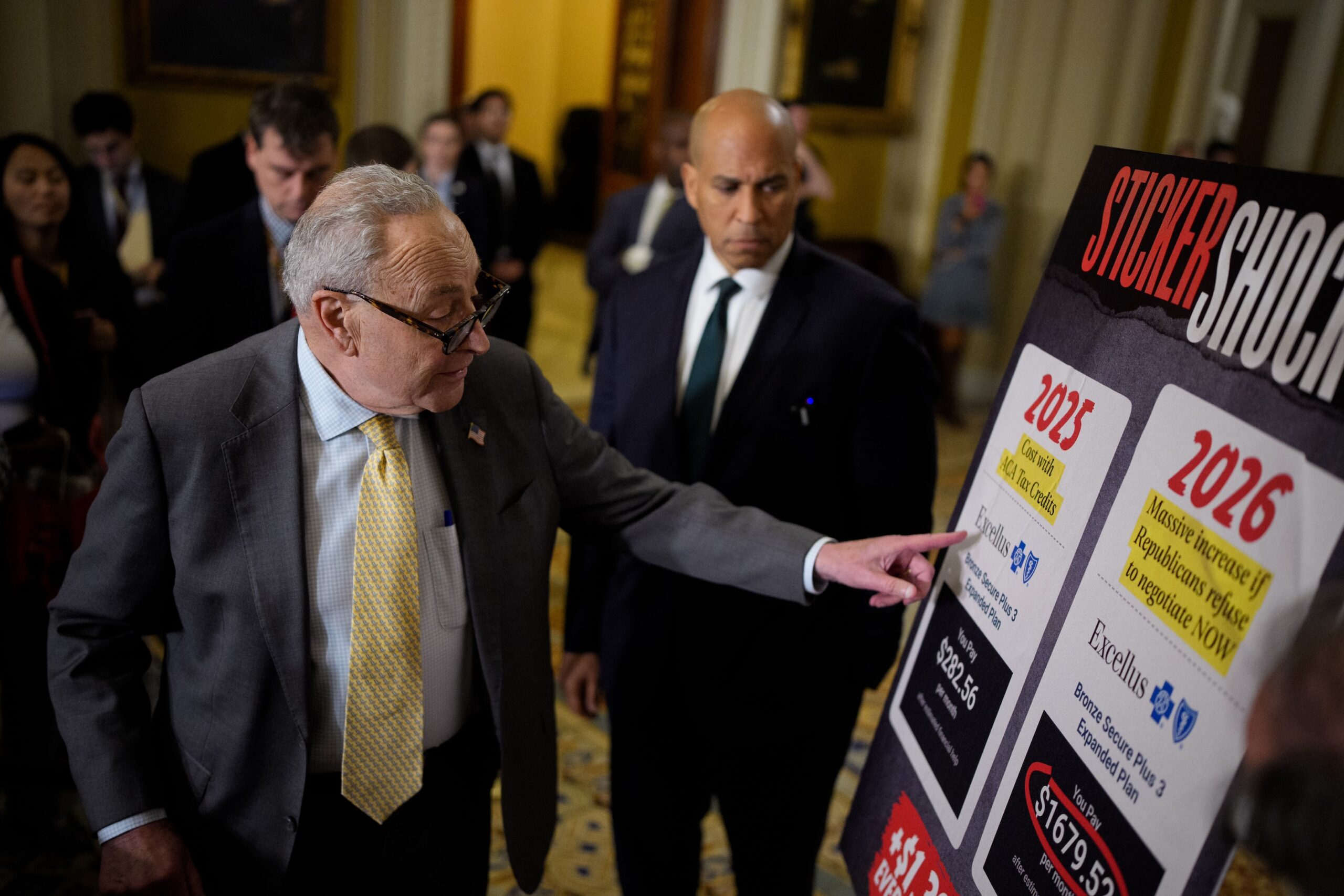 Senate Minority Leader Chuck Schumer, D-N.Y., left, accompanied by Sen. Cory Booker, D-N.J., points to a poster depicting rising medical costs if Congress allows the Affordable Care Act tax credits to expire, at the U.S. Capitol on Oct. 15, 2025. (Photo by Andrew Harnik/Getty Images)
